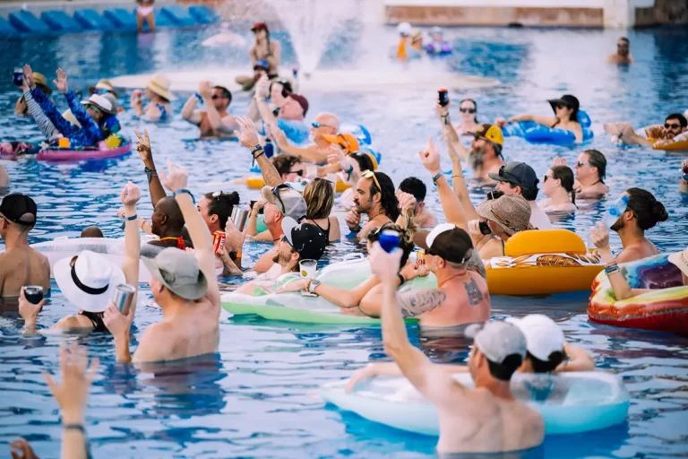 Guests with their hands up in the main pool watching a day time concert.