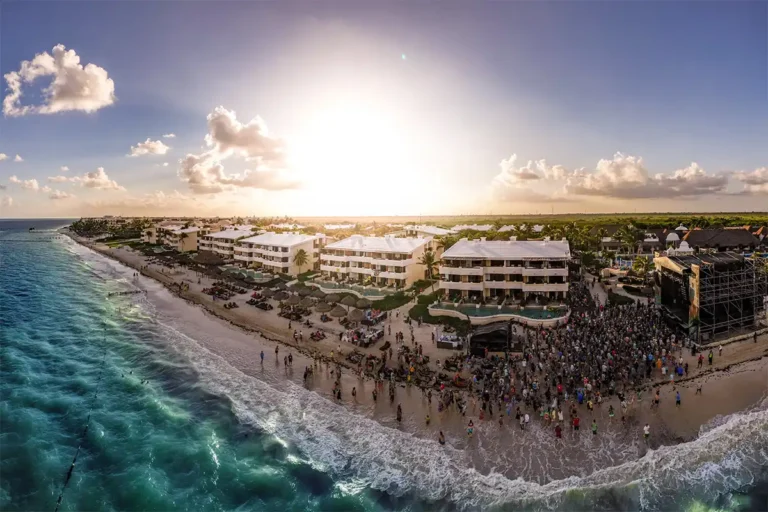 A drone aerial view of the Sapphire resort. A crowd is watching a daytime concert on the beach.