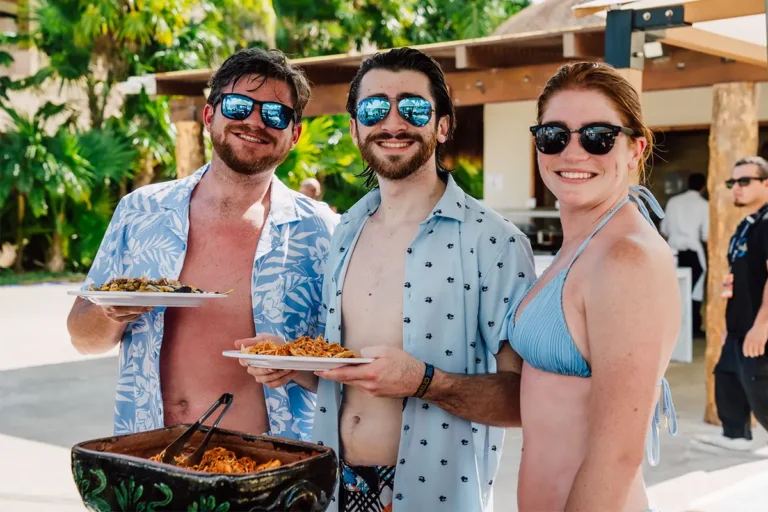 Guests holding up plates of food from a poolside buffet.