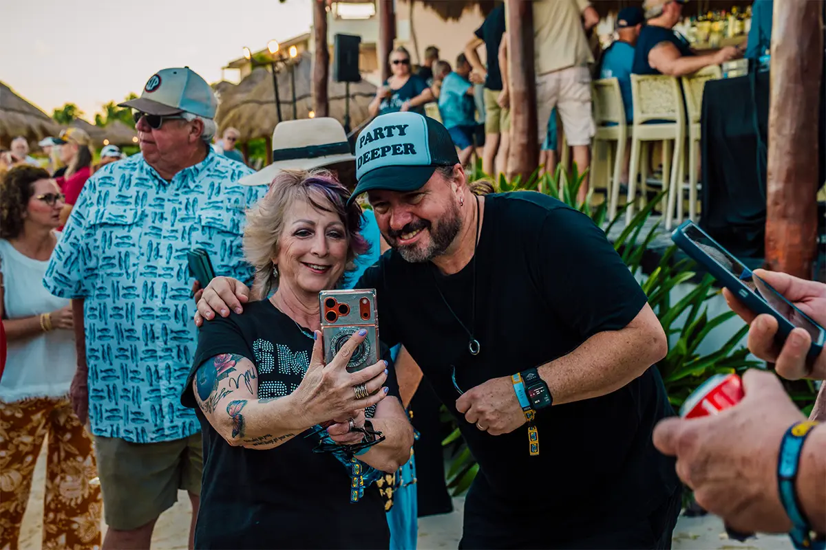 A guest taking a selfie with a member of Blackberry Smoke during a welcome party on the beach.