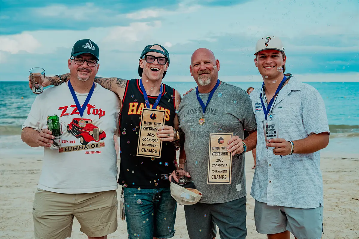 A group photo of guests holding a Cornhole Tournament trophy on the beach.