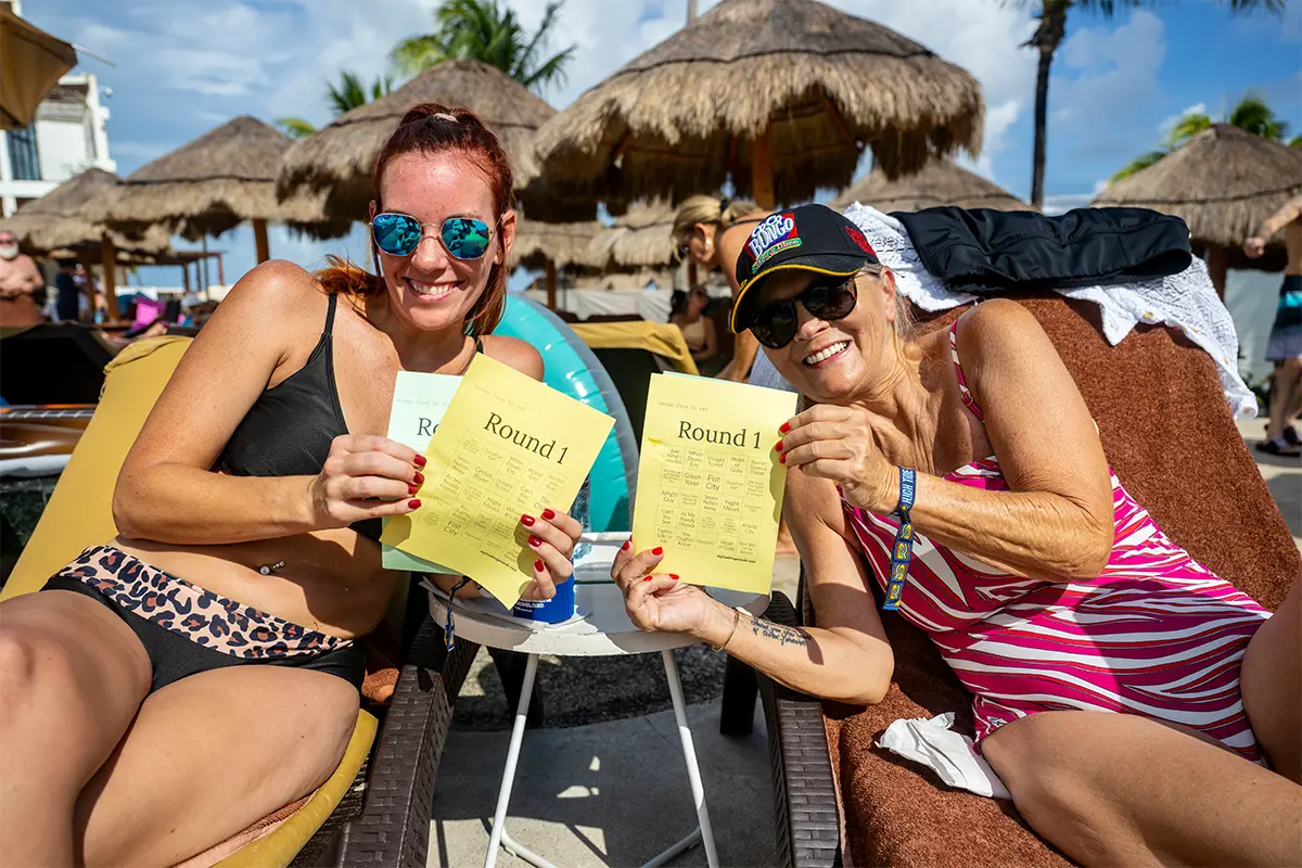 Guests lounging in pool chairs holding up Bingo cards during a poolside activity.